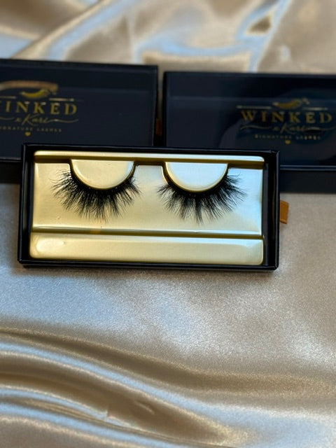 Champagne strip lashes in gold Winked x Kari tray on white satin fabric with black Winked boxes in background