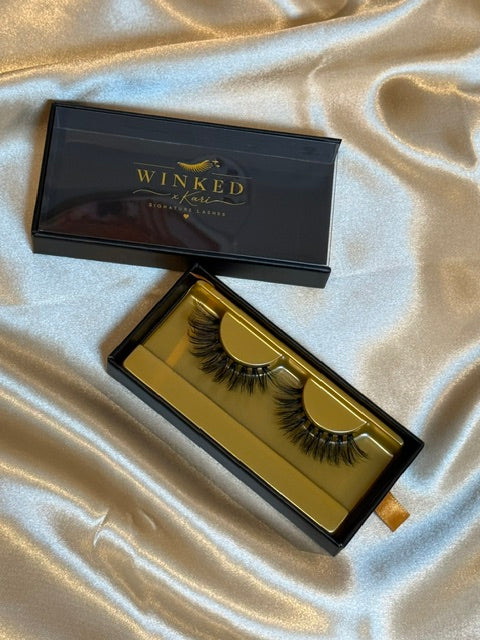 Drama strip lashes in gold Winked x Kari tray inside open black signature lashes box on champagne satin fabric