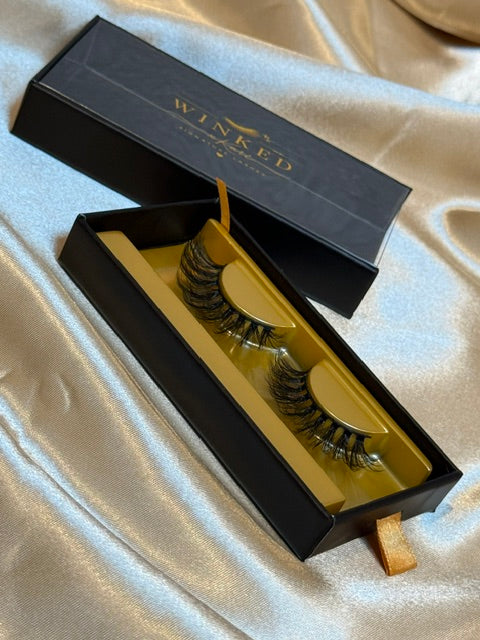 Drama strip lashes close up in gold tray inside open black Winked x Kari signature lashes box showing maximum dramatic volume