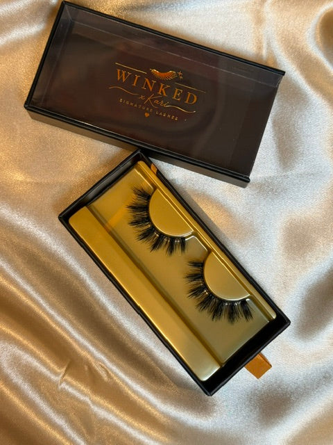 Falsetto strip lashes in gold Winked x Kari tray inside open black signature lashes box on champagne satin fabric