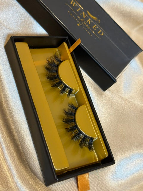 Falsetto strip lashes close up in gold tray inside open black Winked x Kari signature lashes box showing dramatic feathered volume