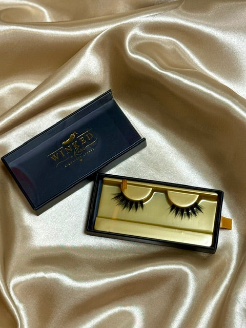 Kiss Me strip lashes with black and gold Winked Rose box open on champagne satin fabric
