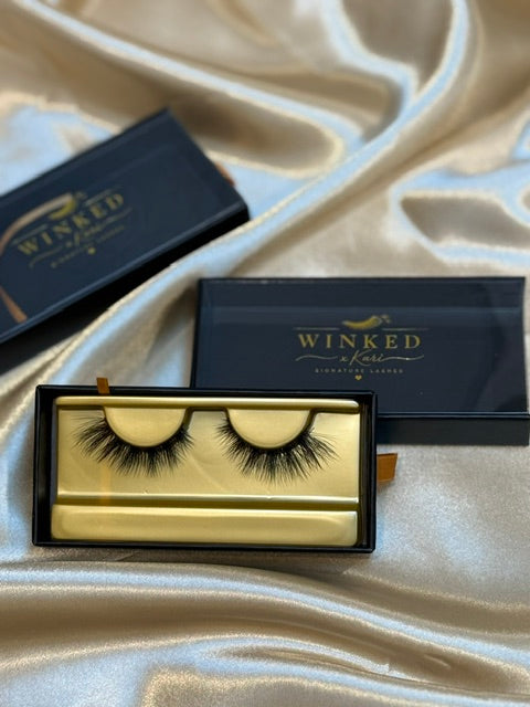 Muse strip lashes in gold Winked x Kari tray with black box lid open on white satin fabric