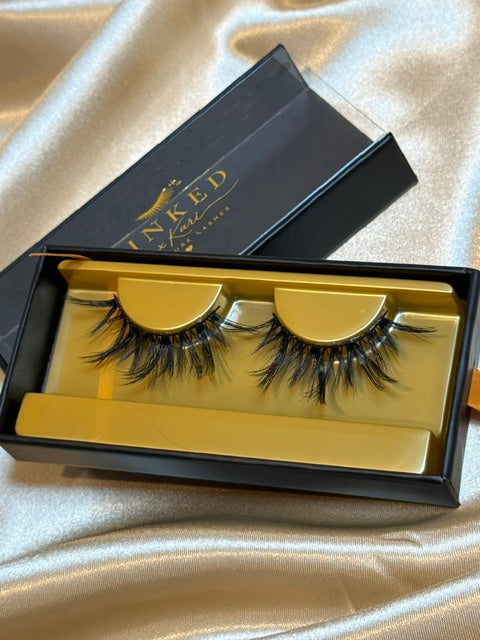 Mystique strip lashes in gold Winked x Kari tray inside open black signature lashes box on white satin fabric