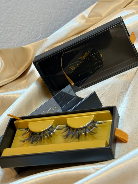 Mystique strip lashes in gold tray inside open black Winked x Kari signature lashes box on champagne satin fabric