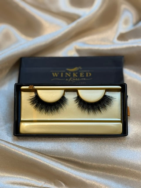 Noir strip lashes in open black and gold Winked x Kari box on white satin fabric
