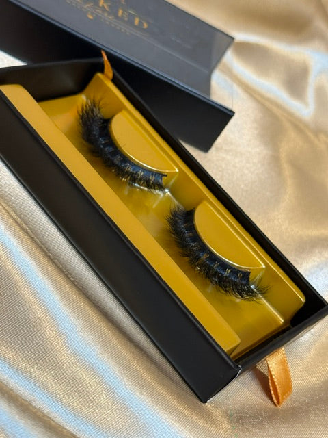 Runway strip lashes close up in gold tray inside open black Winked x Kari signature lashes box showing editorial feathered volume