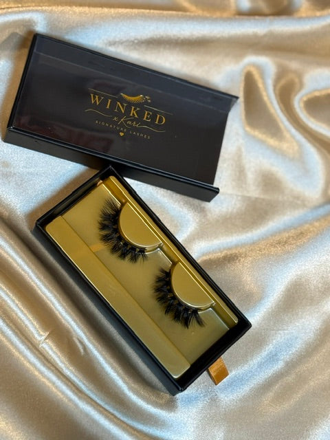 Savage strip lashes in gold Winked x Kari tray inside open black signature lashes box on white satin fabric