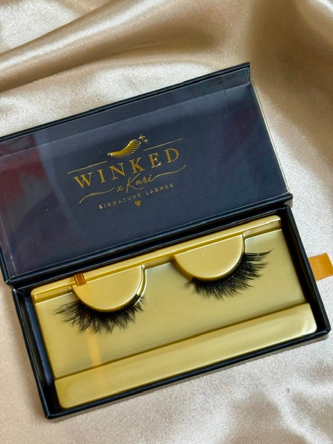 Sinful strip lashes in open black and gold Winked x Kari signature lashes box on satin fabric