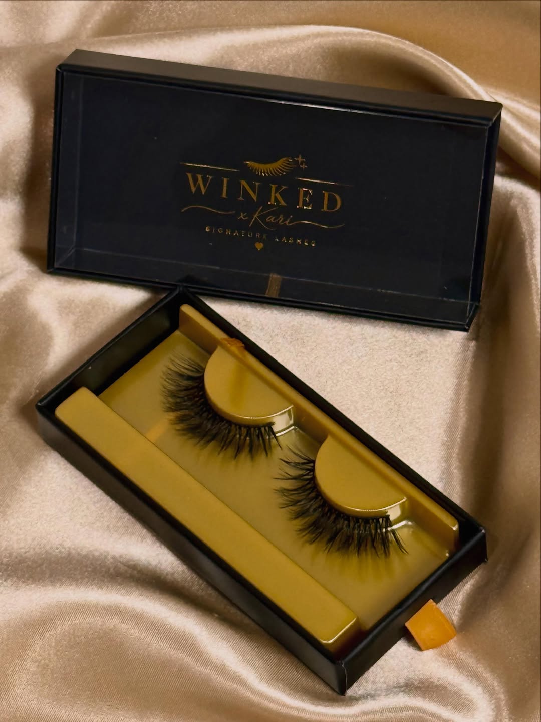 Trinity false eyelashes in black packaging with a gold interior tray on draped satin